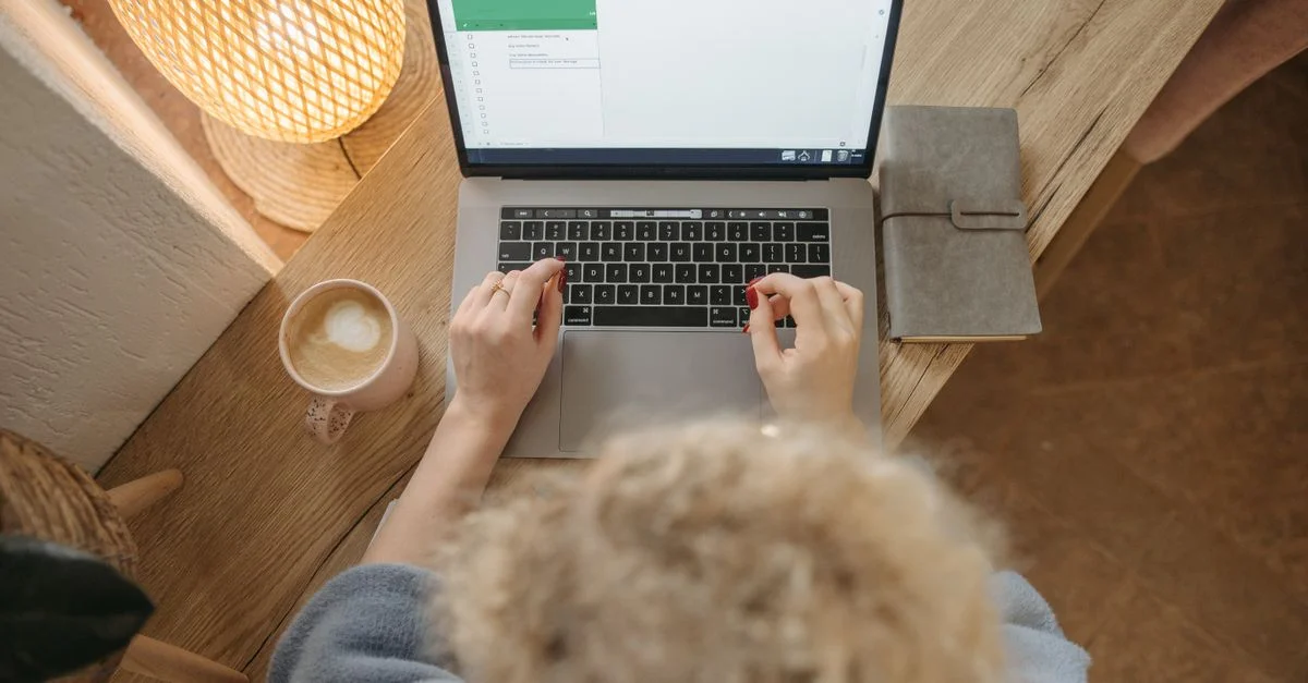 Vue aérienne d'une personne travaillant sur un ordinateur portable avec du café et un journal sur un bureau en bois.