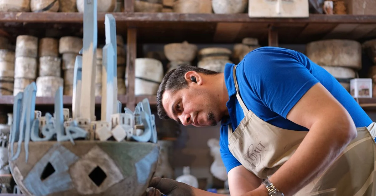 Un artisan concentré sculptant des œuvres d'art détaillées dans un atelier rempli de matériaux et d'outils.