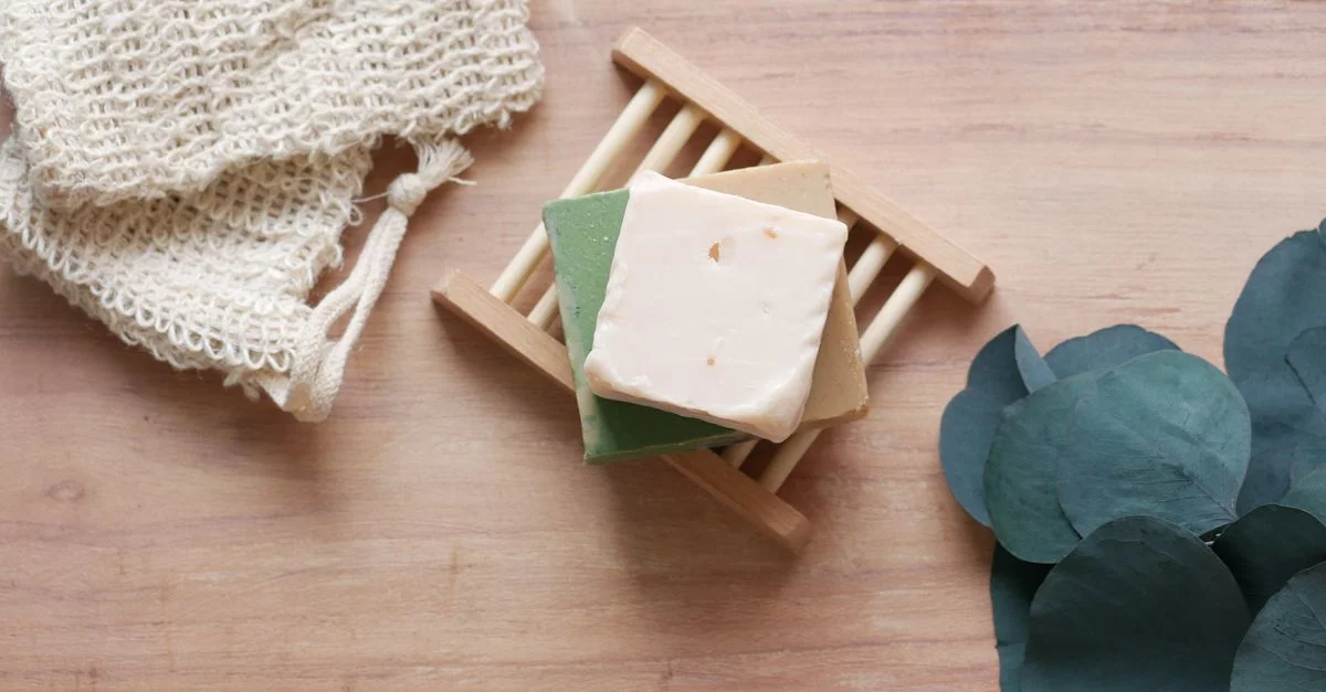 Vue de dessus de barres de savon fait main sur un plat en bambou avec des feuilles vertes, avec un fond en bois rustique.