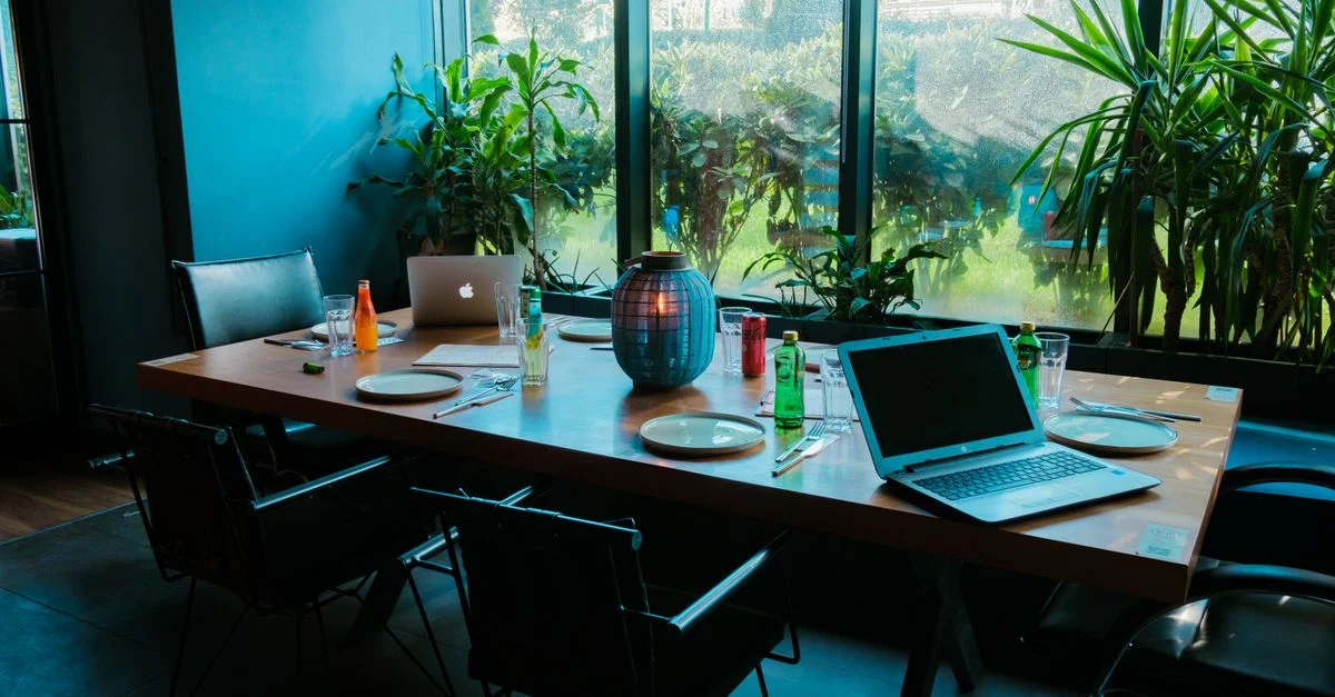 Salle de réunion moderne avec ordinateurs portables, boissons et verdure luxuriante.