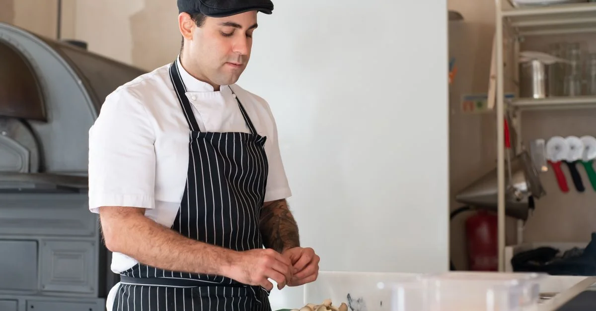 Un chef en tenue traditionnelle prépare de la nourriture dans un cadre de cuisine, montrant ses compétences culinaires.