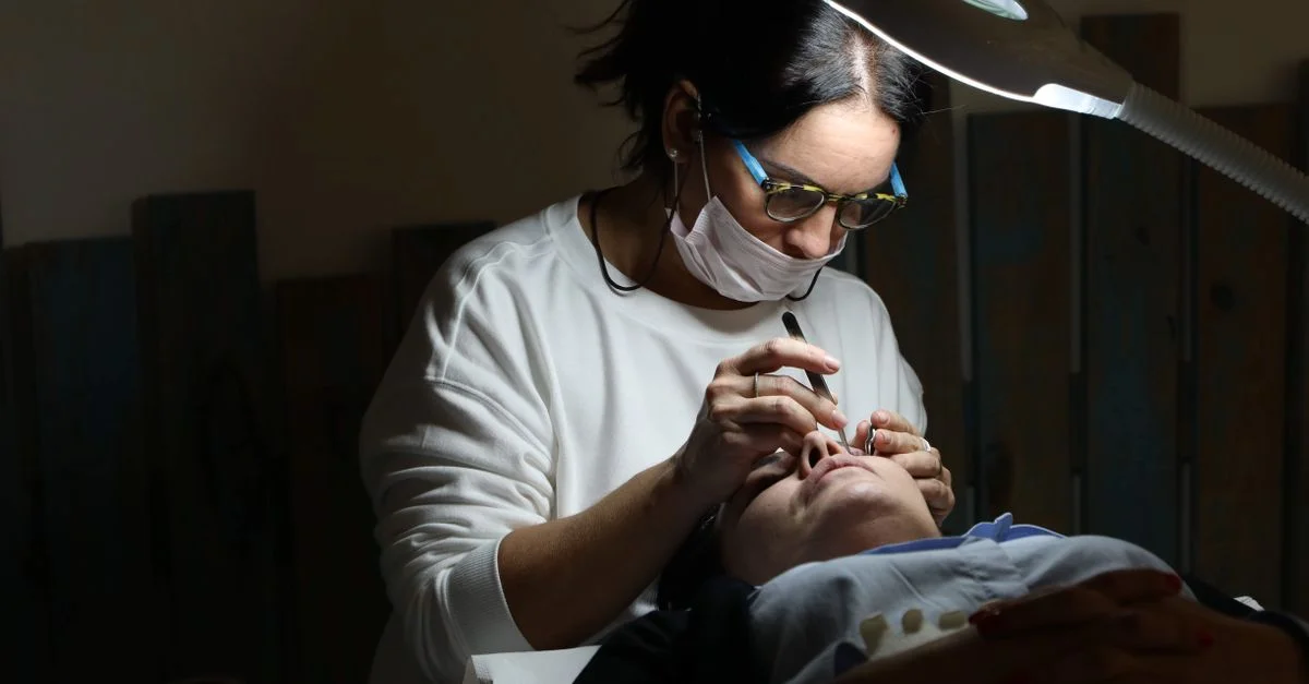 Une esthéticienne professionnelle applique des extensions de cils dans un salon, sous un éclairage ciblé.
