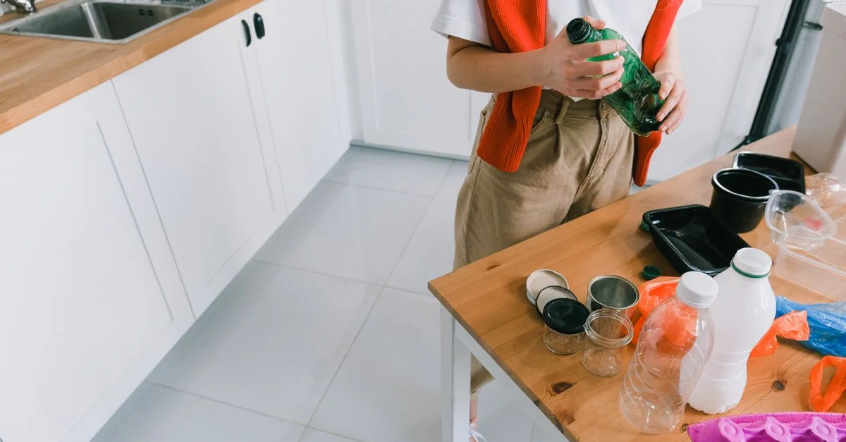 Une femme trie divers conteneurs recyclables sur une table de cuisine avec des plans de travail en bois.