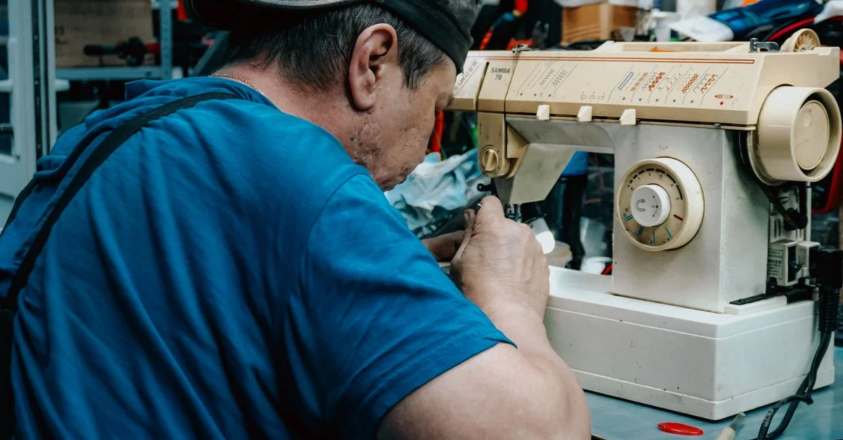 Un homme concentré, occupé à réparer une machine à coudre ancienne, fait preuve d'un savoir-faire exceptionnel dans son atelier.