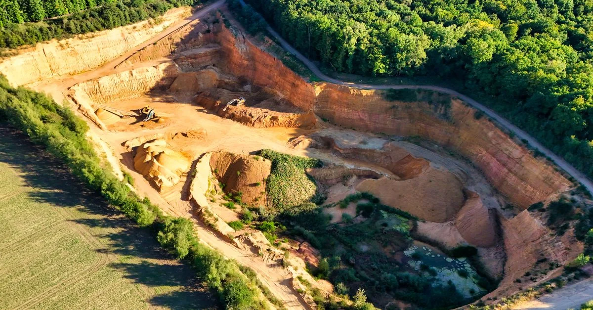 Une magnifique vue aérienne d'une grande carrière en contraste avec de luxuriantes forêts vertes.
