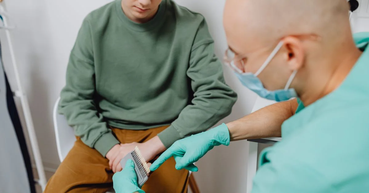 Un dentiste masqué montre des options dentaires à un jeune patient dans une clinique.