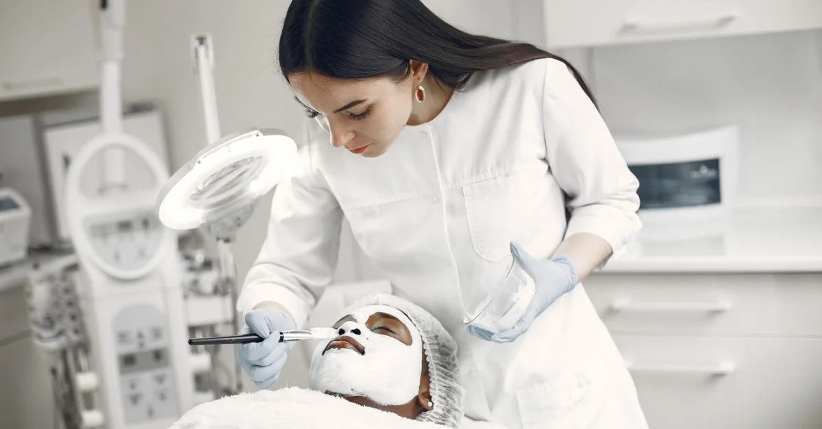 Une esthéticienne applique un masque facial à une cliente dans une clinique de beauté, axée sur les soins de la peau et la détente.