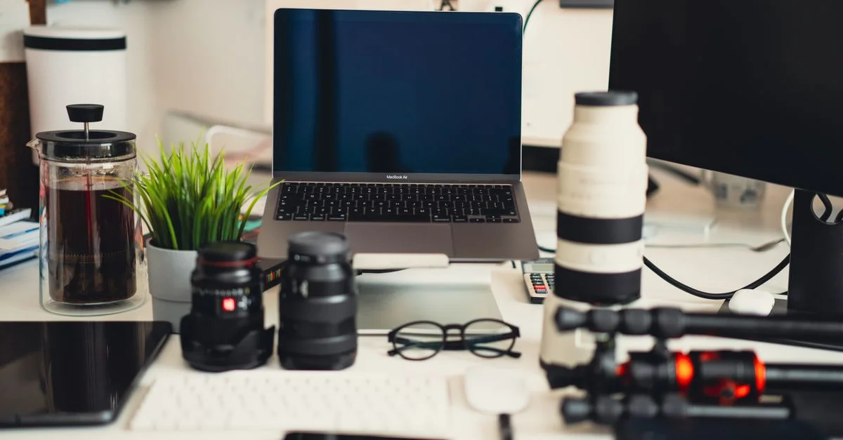 Configuration de bureau moderne avec ordinateur portable, objectifs et matériel de photographie.