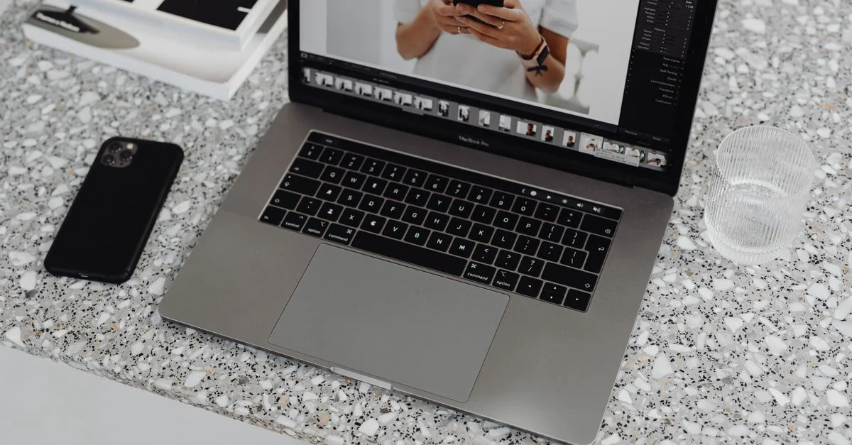 Un ordinateur portable élégant et un smartphone sur une surface en marbre stylée avec un verre d'eau à proximité.