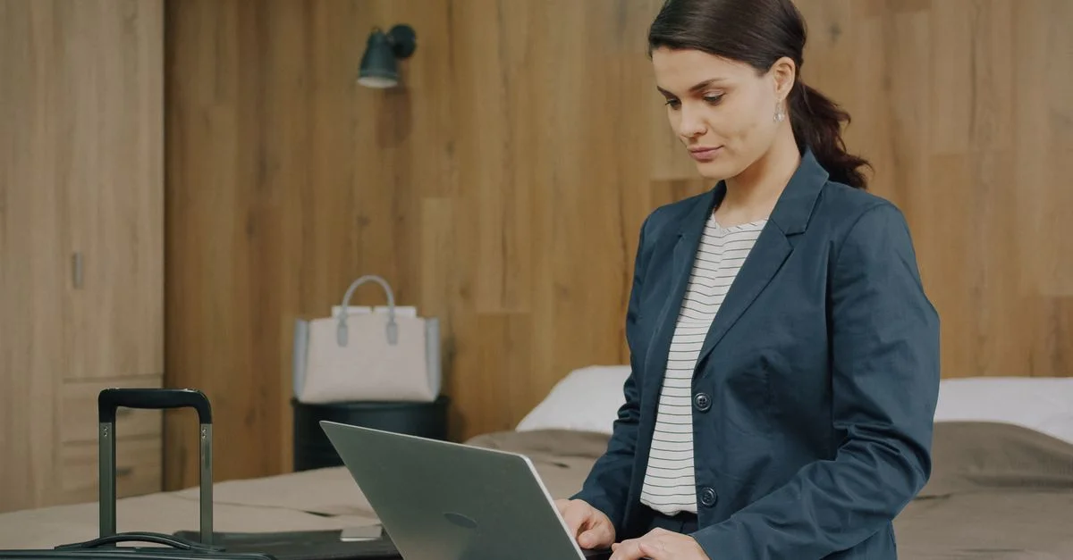 Femme active utilisant un ordinateur portable dans une chambre d'hôtel, se préparant pour un voyage d'affaires.