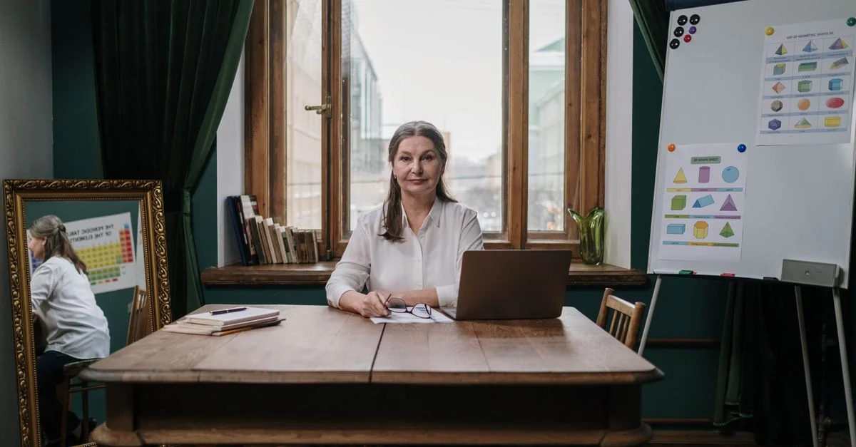 Femme âgée enseignant avec un ordinateur portable dans un bureau à domicile, montrant des graphiques et des supports éducatifs.