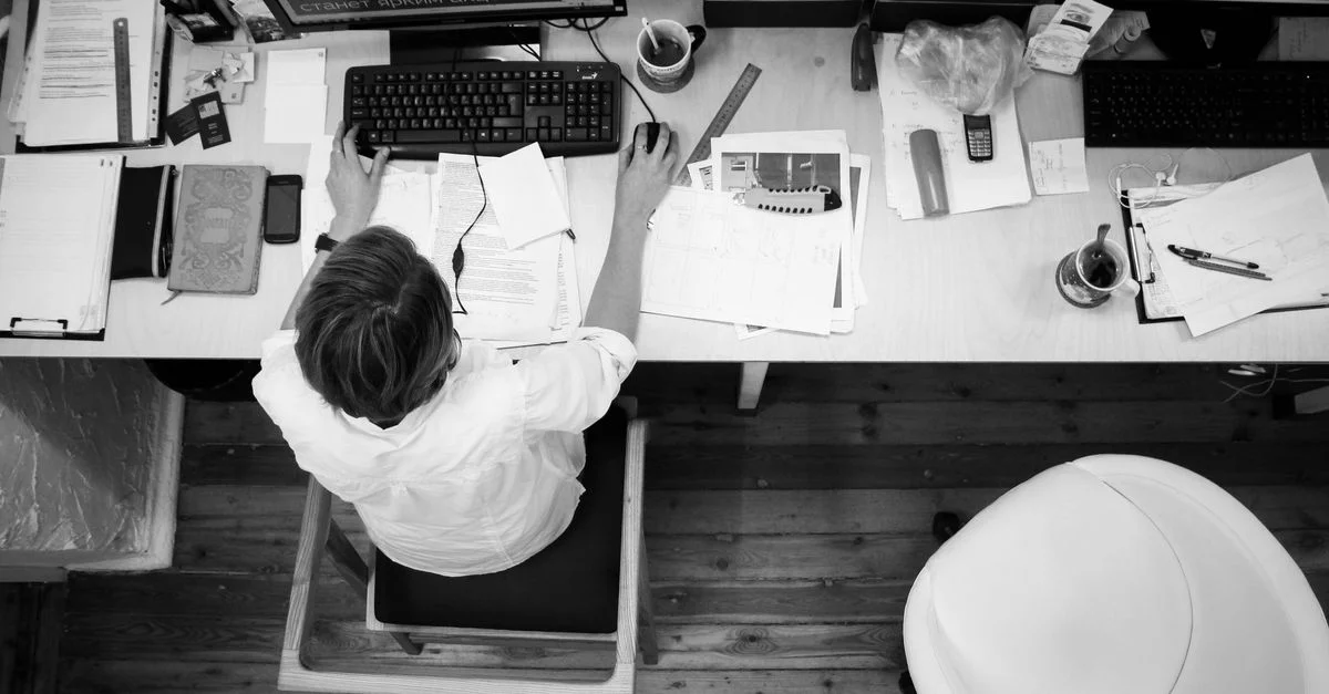 Image en noir et blanc d'un employé travaillant à un bureau avec des papers et un ordinateur.