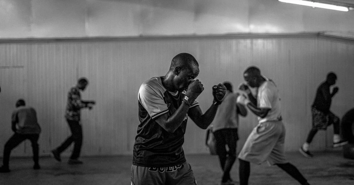 Photo en noir et blanc de boxeurs s'entraînant dans une salle de sport intérieure, capturant une concentration et un mouvement intenses.