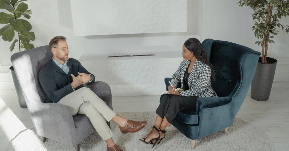 Deux professionnels engagés dans un entretien, assis sur des fauteuils dans un cadre de bureau moderne.