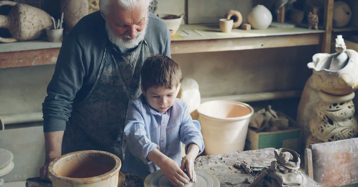 Un homme âgé guide un jeune garçon dans la fabrication de poteries dans un atelier rustique.