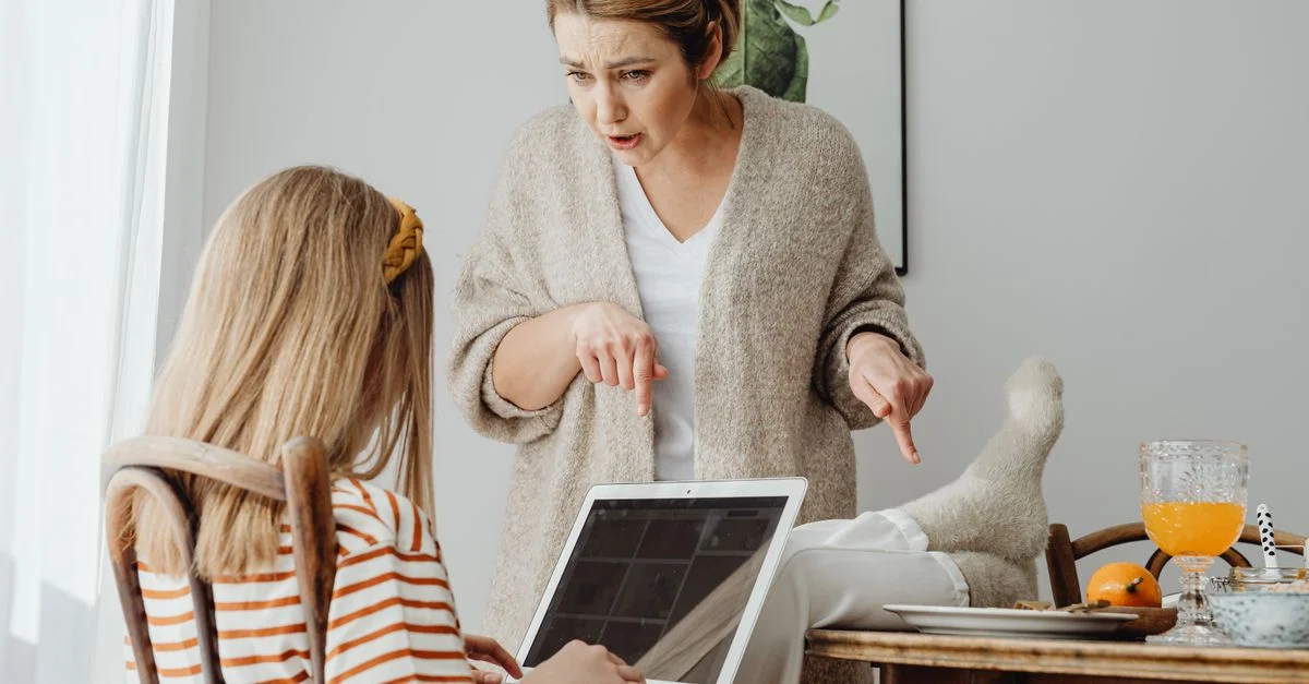 Une mère réprimande sa fille adolescente qui utilise un ordinateur portable à la maison, mettant en avant un conflit générationnel.