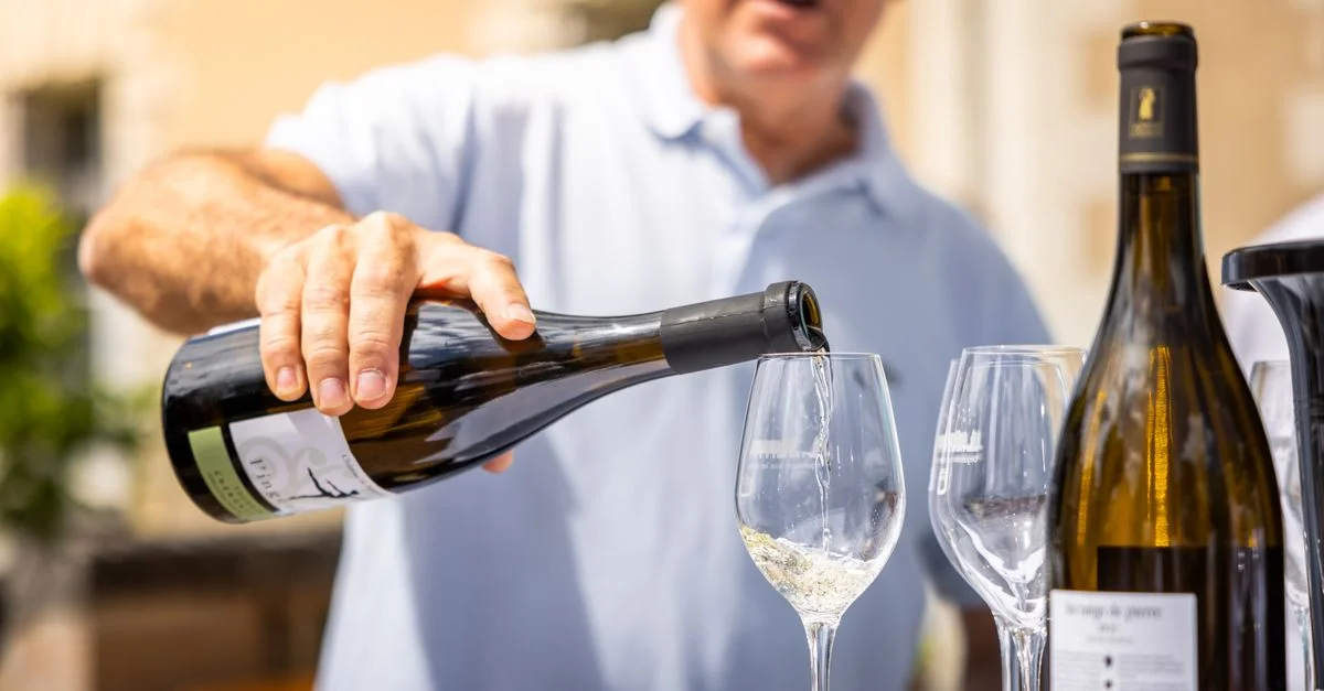 Un adulte verse du vin blanc dans un verre à l'extérieur lors d'une dégustation de vins.