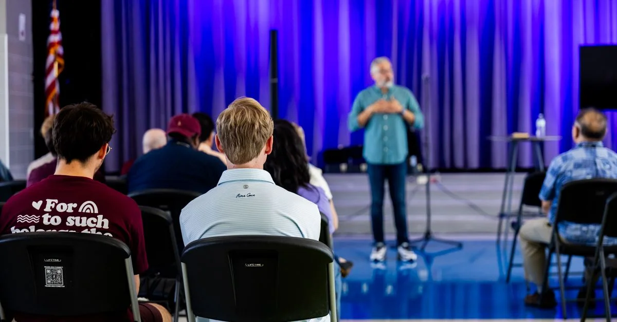 Des personnes écoutant un conférencier dans une salle éclairée en bleu, manifestent leur intérêt et leur engagement.