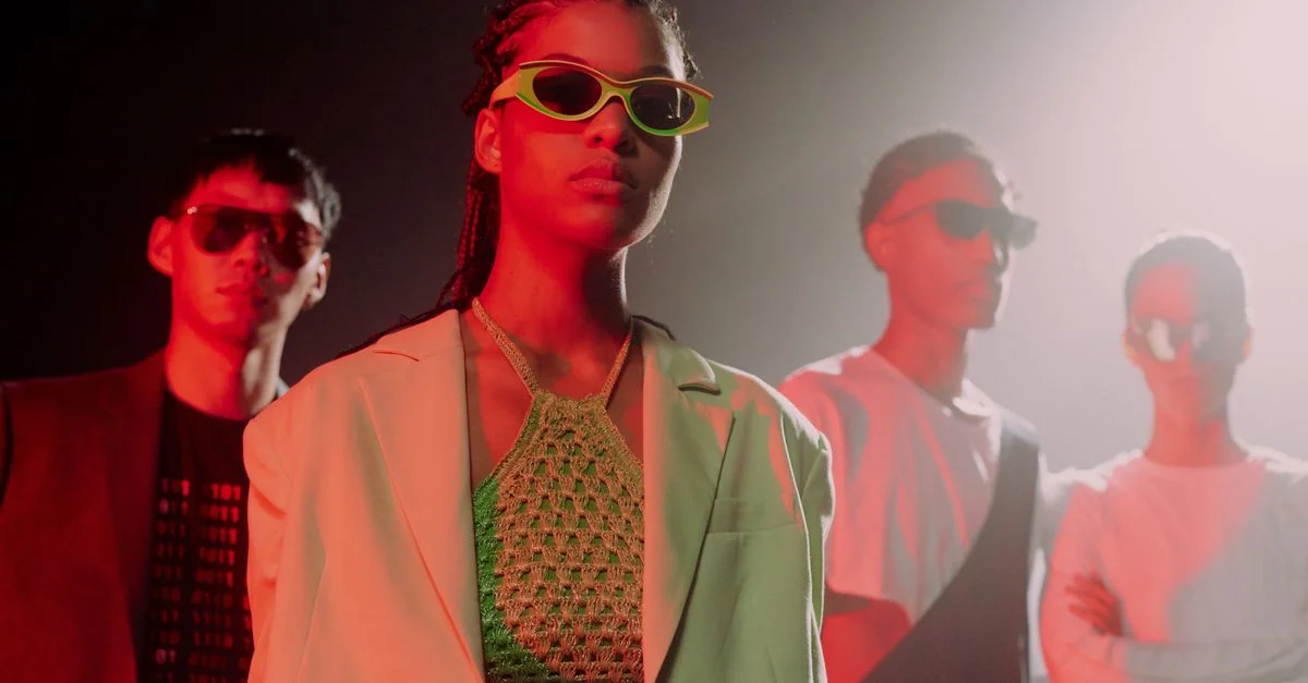 Un groupe élégant de jeunes mannequins portant des lunettes de soleil pose sous un éclairage de studio vibrant, mettant en valeur des vêtements de rue modernes.