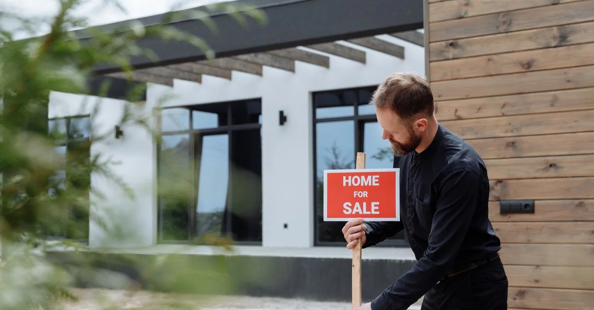 Homme plaçant un panneau à vendre devant une maison moderne pour une annonce immobilière.