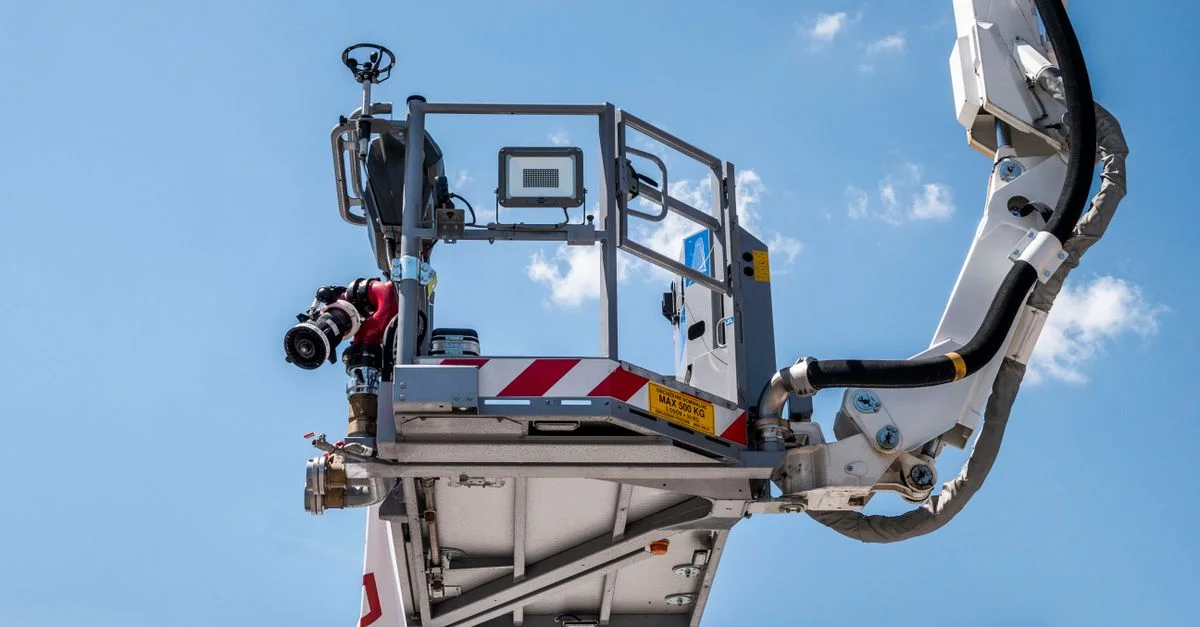Camion de pompier équipé d'une échelle, d'un canon à eau et d'un tuyau sous un ciel bleu.