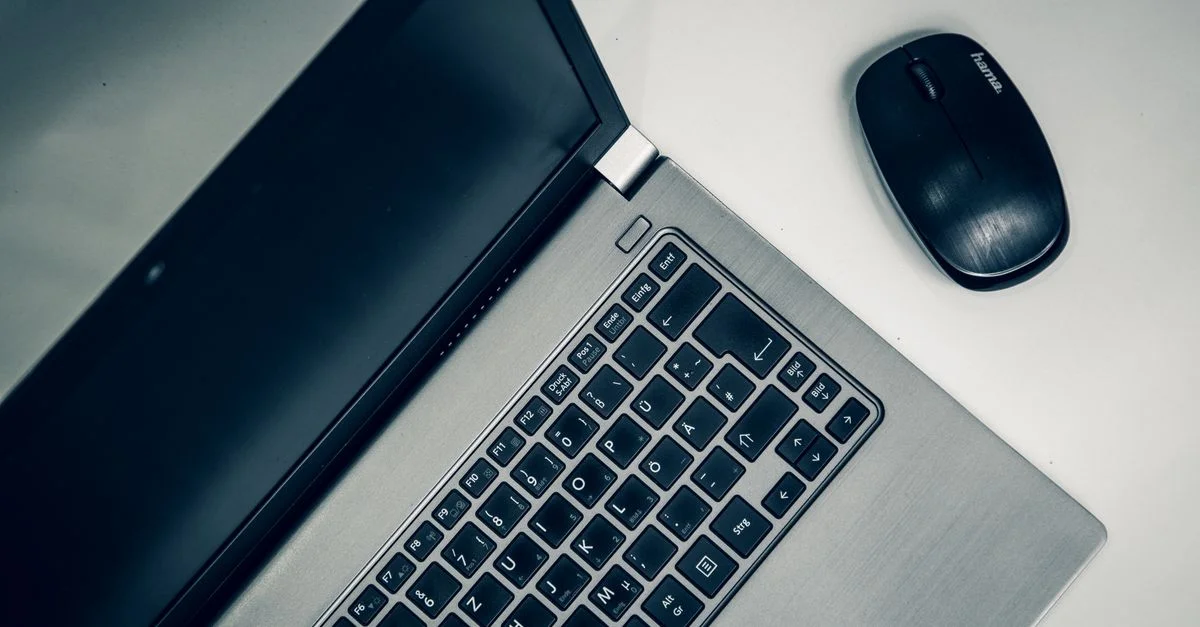 Une vue rapprochée d'un ordinateur portable argenté et d'une souris sans fil sur une table lisse, idéale pour les aménagements de bureau à domicile.