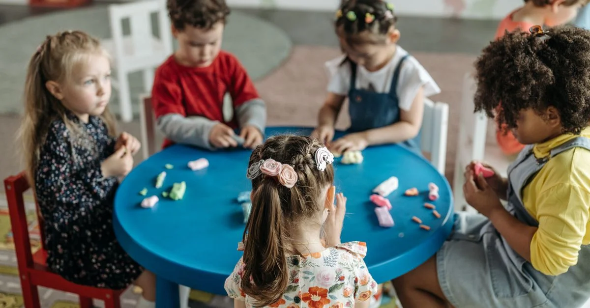Groupe d'enfants d'âge préscolaire jouant avec de la pâte à modeler à une table colorée dans une salle de classe.