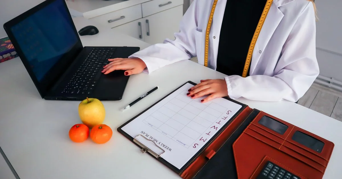 Diététicienne travaillant sur un plan de repas avec un ordinateur portable, des fruits et un calendrier pour une consultation santé.
