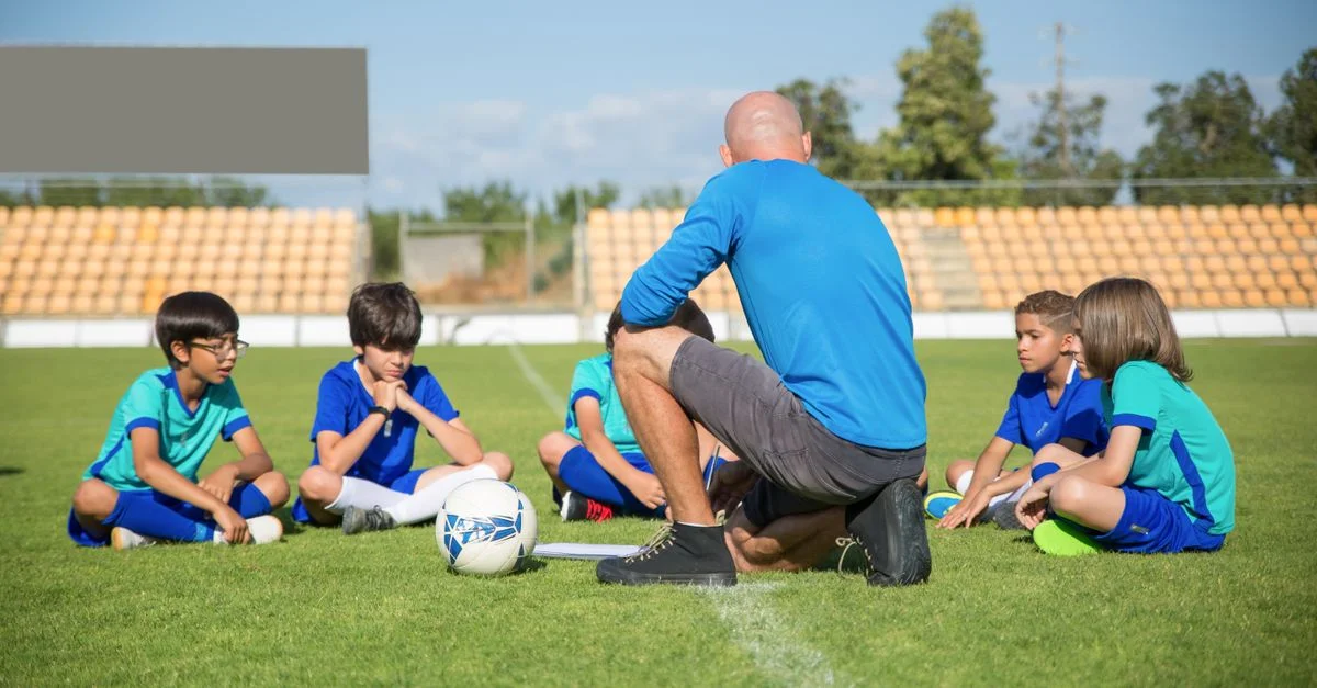 Groupe d'enfants recevant un entraînement de football par une journée ensoleillée sur un terrain de football au Portugal.