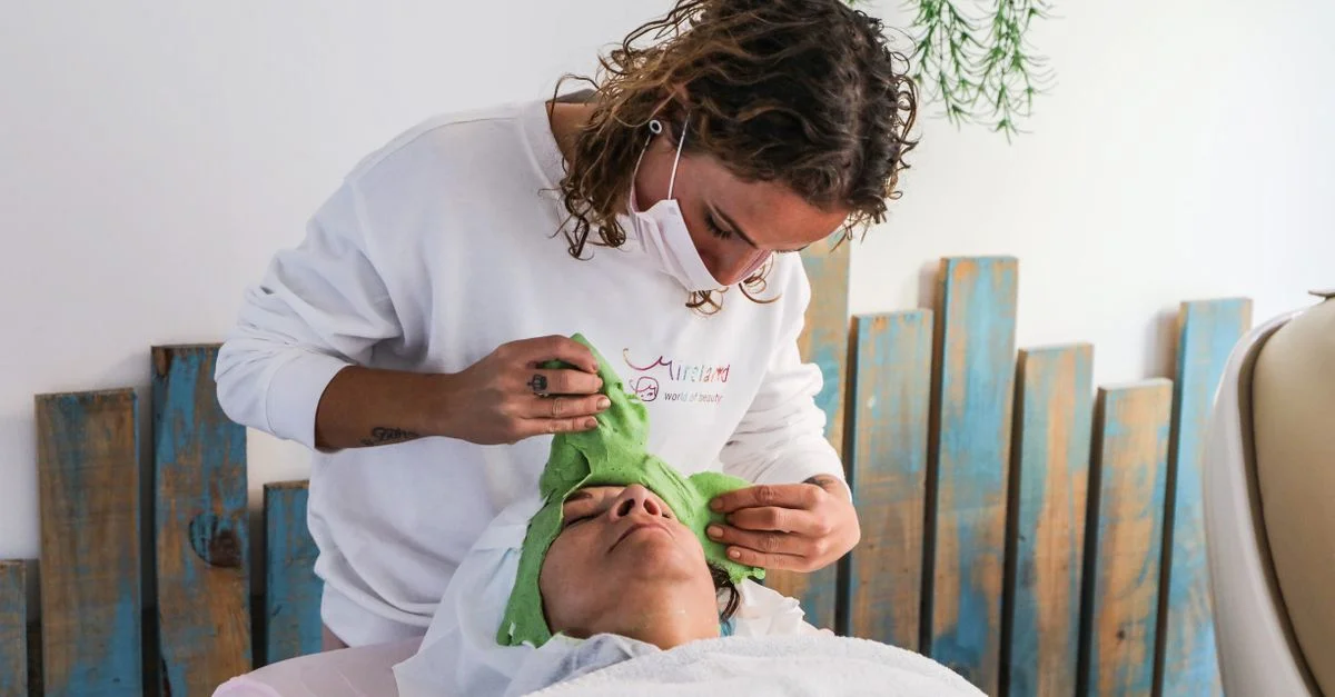 Une esthéticienne applique un masque facial vert lors d'un soin relaxant au spa.