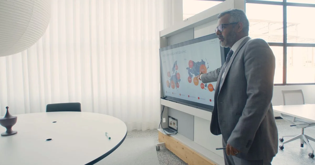 Professionnel en costume présentant des données sur un écran dans un environnement de bureau moderne.