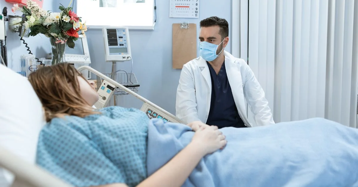 Un médecin portant un masque facial parle à un patient dans un lit d'hôpital, fournissant des soins et des consultations.
