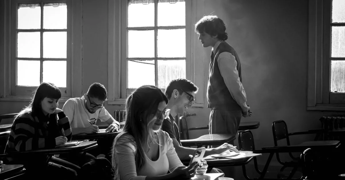 Image en noir et blanc d'étudiants étudiant dans une salle de classe avec un enseignant présent.