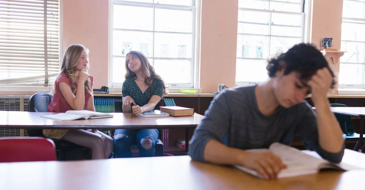 Des étudiants assis à des bureaux dans une salle de classe, se concentrant sur des livres et des discussions.