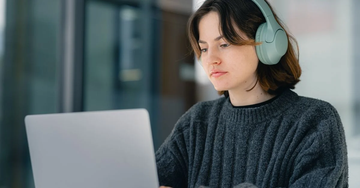 Jeune femme portant des écouteurs travaillant sur un ordinateur portable à l'intérieur, concentrée et engagée.