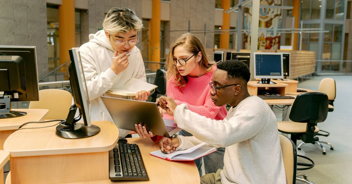 Un groupe d'étudiants travaillant ensemble sur un ordinateur portable dans un cadre de bibliothèque moderne.