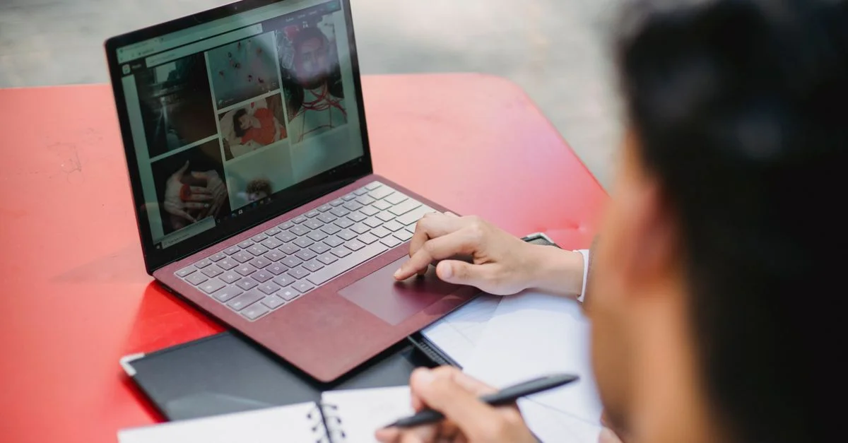 Personne travaillant sur un ordinateur portable et prenant des notes sur une table rouge à l'extérieur.