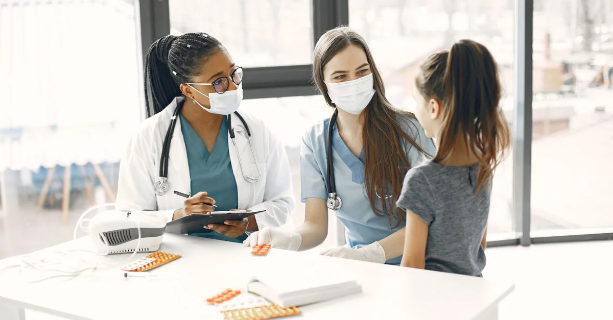 Deux médecins féminines masquées assistent un enfant dans une salle médicale lumineuse.
