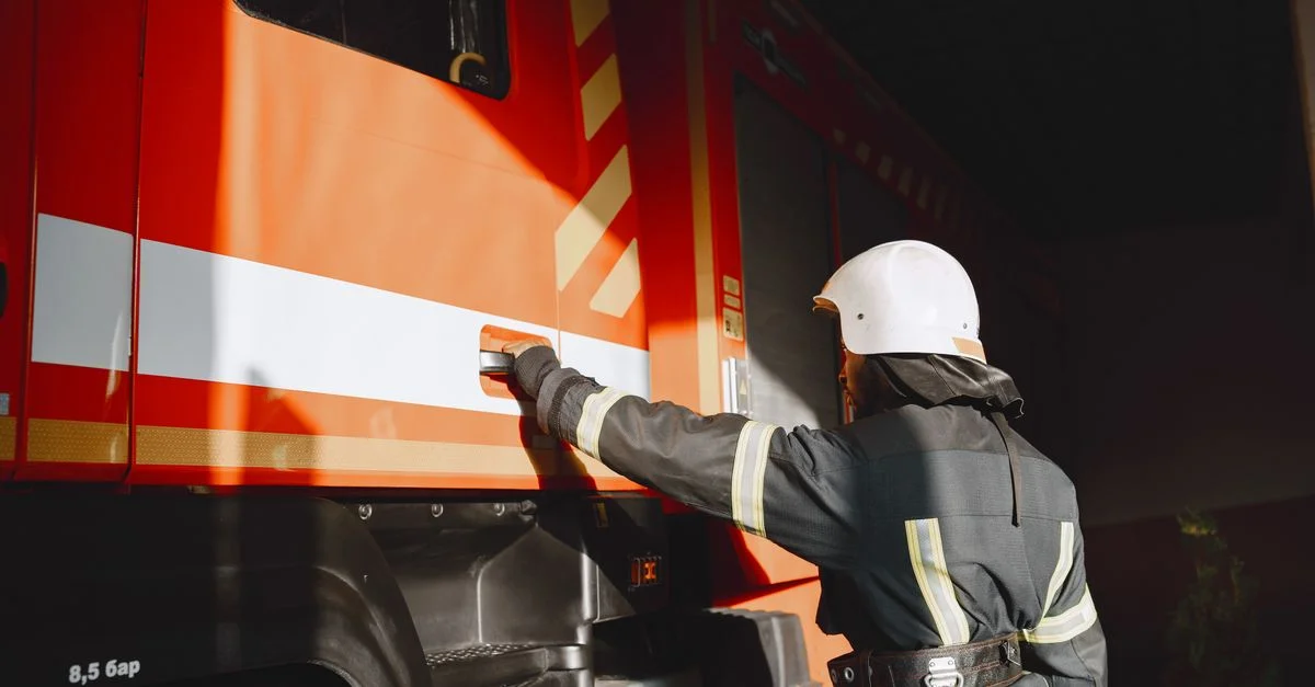 Pompier en équipement de sécurité travaillant avec un camion de pompiers en plein air pendant la journée.