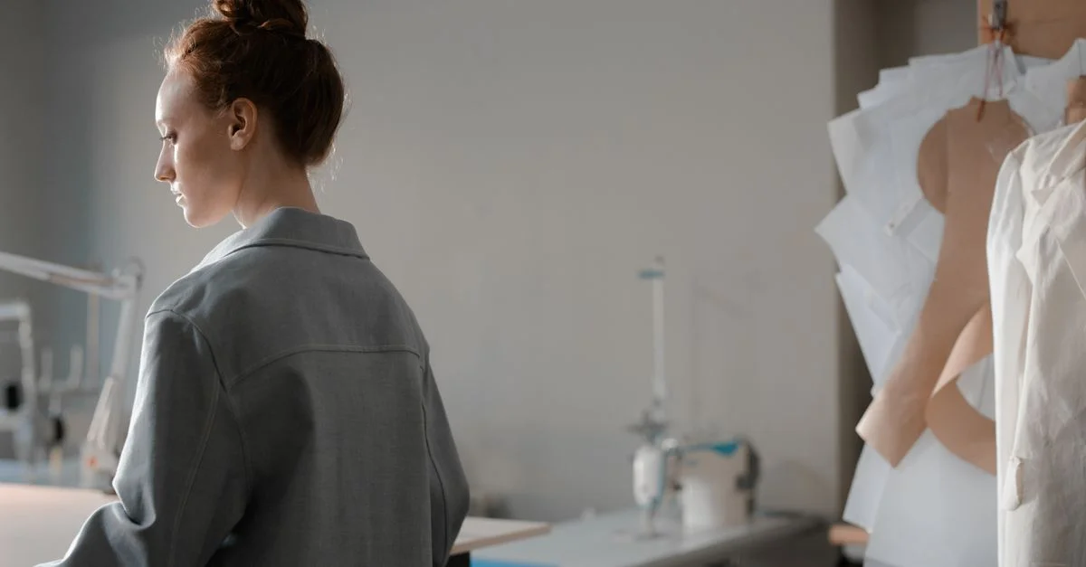 Femme dans un studio de mode examinant des patrons de couture à côté de sa machine à coudre.