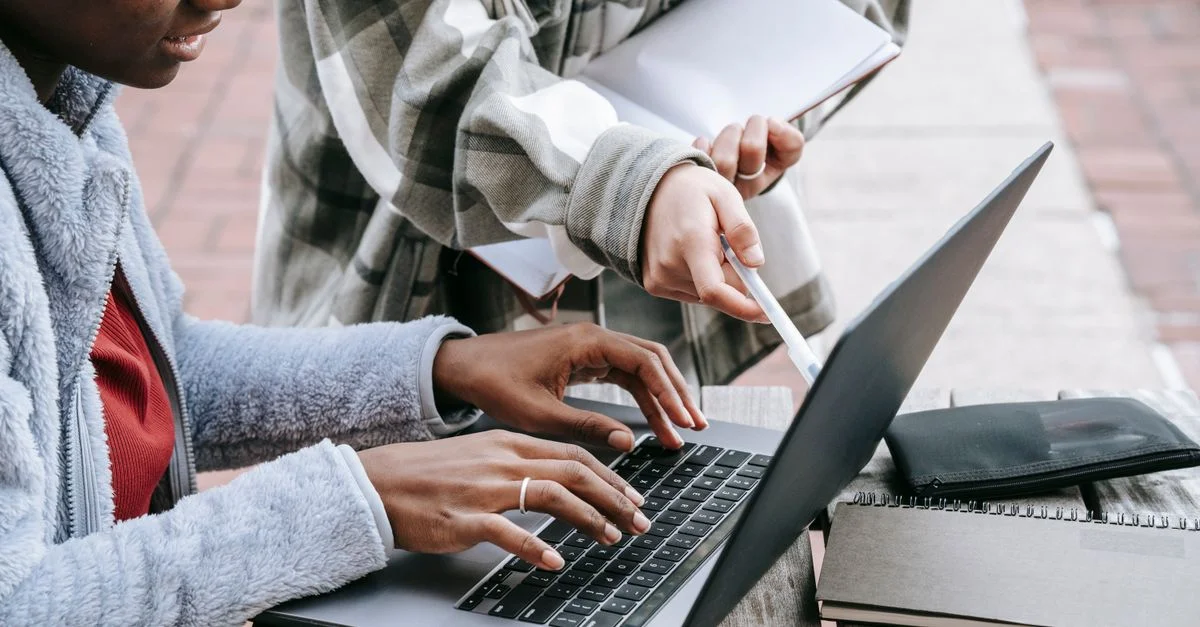 Deux étudiantes collaborent sur un ordinateur portable à l'extérieur, se concentrant sur un projet ensemble.