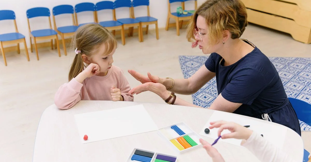 Un enseignant aide un enfant dans une activité de modelage d'argile dans une salle de classe lumineuse de maternelle.