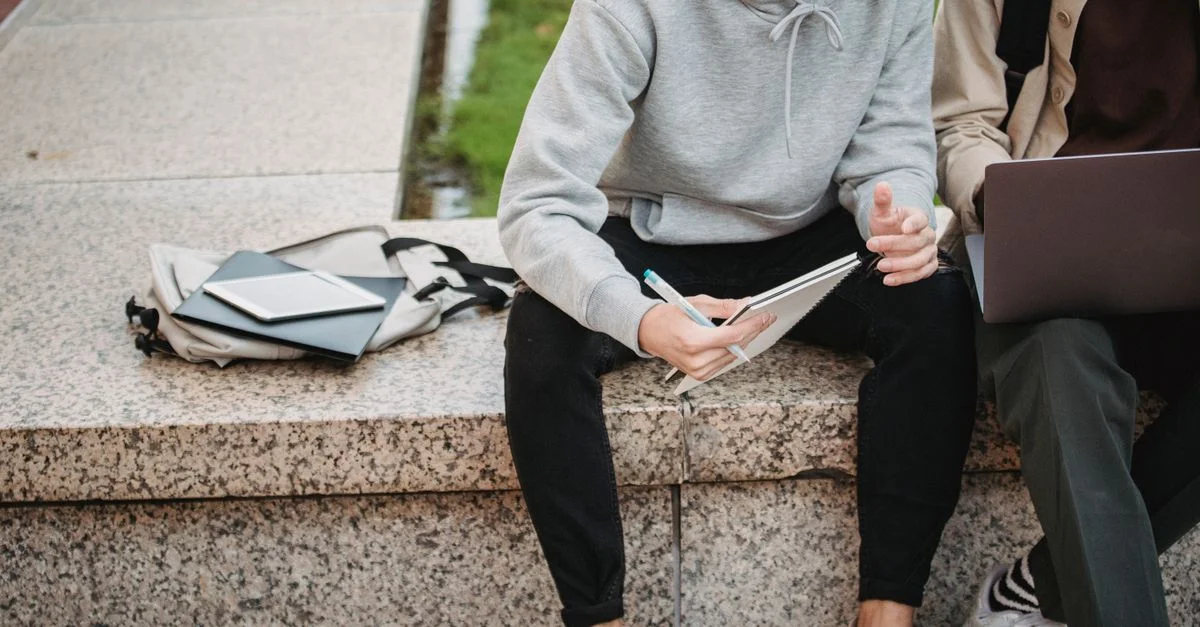 Deux jeunes adultes discutent de travail à l'extérieur tout en utilisant un ordinateur portable et un carnet.