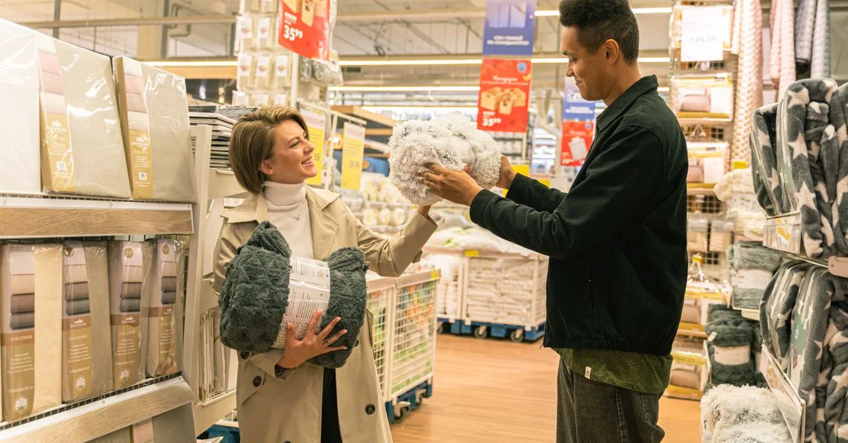 Deux adultes sourient en faisant du shopping pour des textiles dans un magasin de détail, engagés dans une conversation amicale.