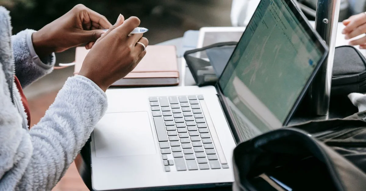 Vue en gros plan de personnes travaillant en collaboration avec des ordinateurs portables et des cahiers à une table en extérieur.
