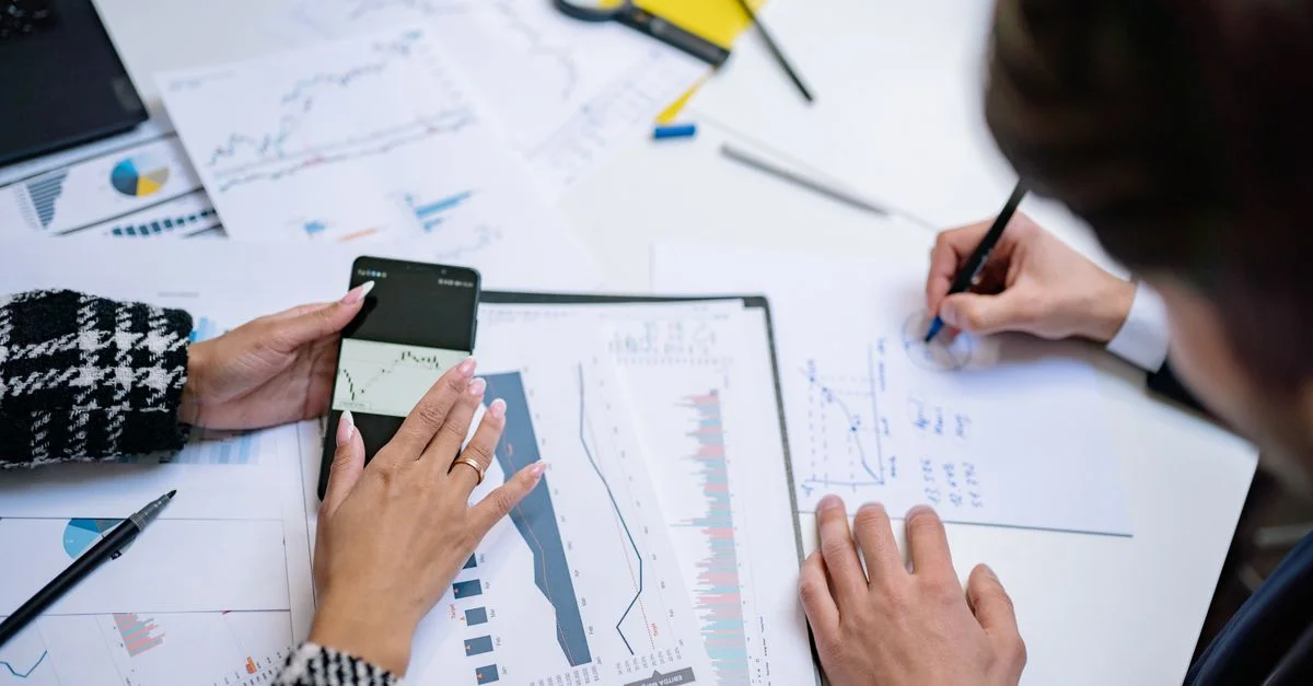 Vue de dessus de personnes analysant des graphiques financiers et des données avec un smartphone et des documents.