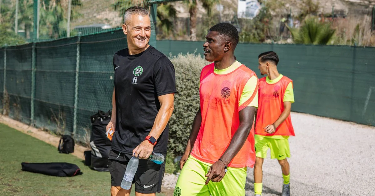 L'entraîneur et les joueurs profitent d'une séance d'entraînement de football en plein air sous un soleil radieux.