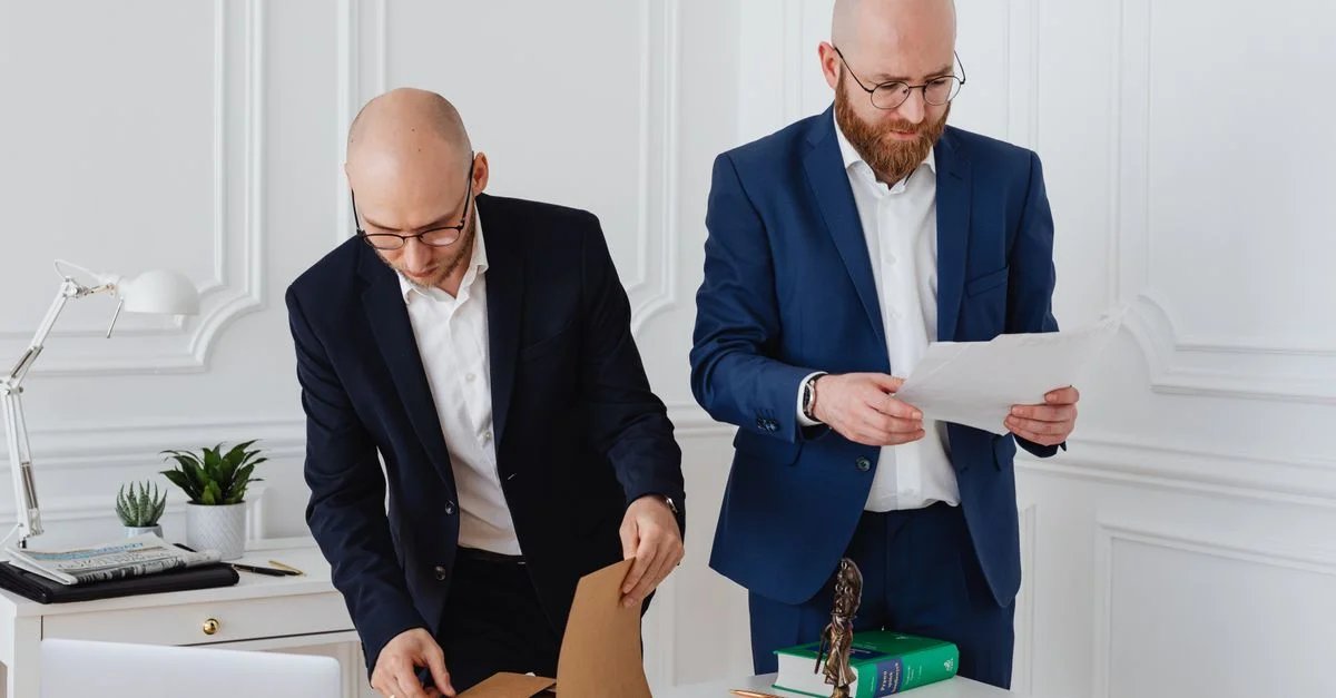 Deux professionnels en affaires en tenue corporative examinant des documents dans un environnement de bureau moderne.