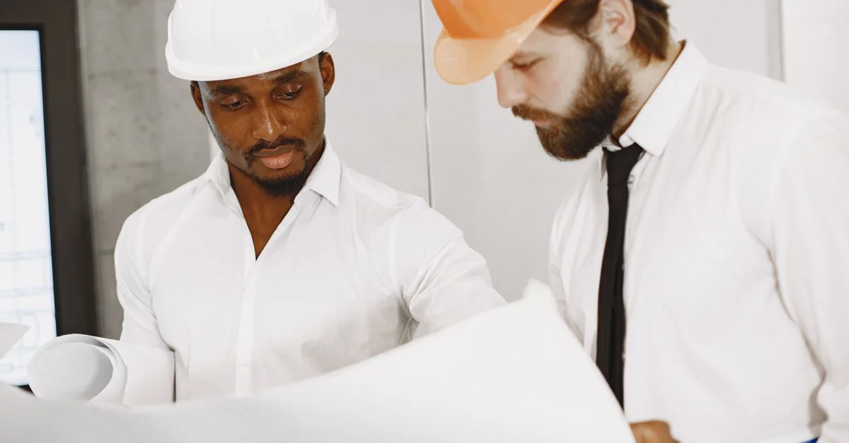 Deux ingénieurs en casques se concentrent sur la révision de plans de construction détaillés à l'intérieur.