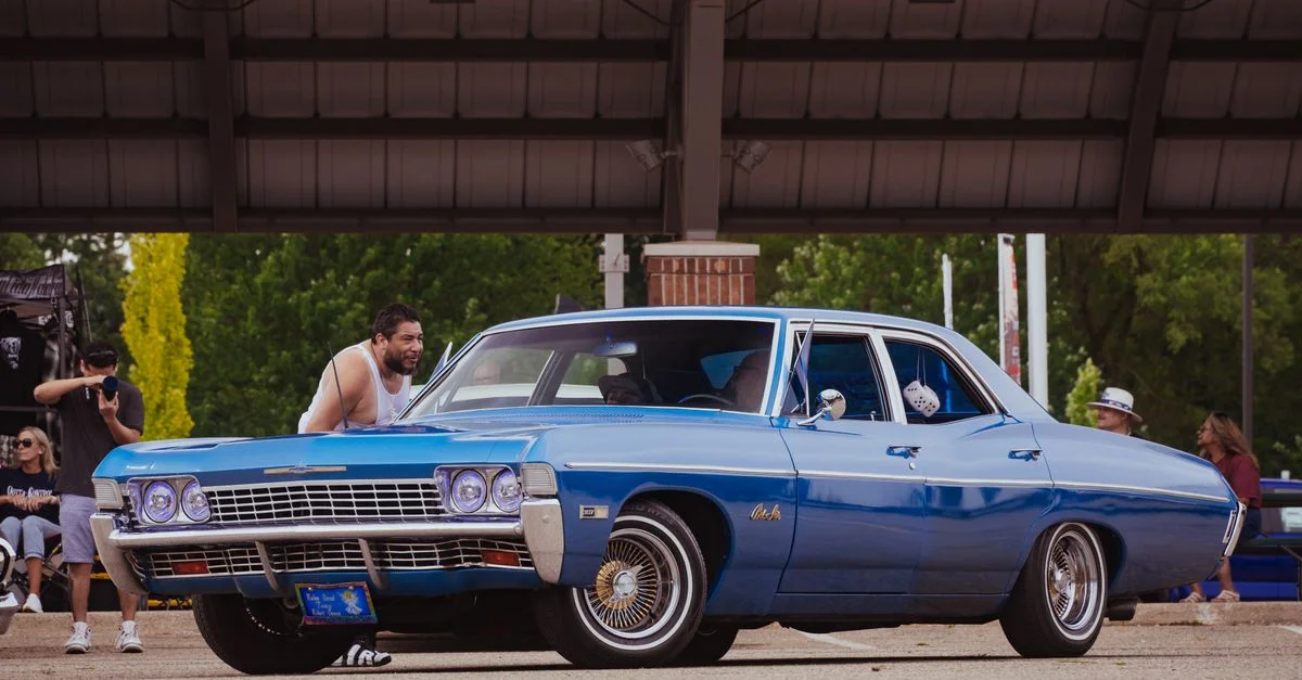 Une vibrante voiture Chevrolet vintage bleue exposée lors d'un salon de voitures en plein air avec des personnes admirant.